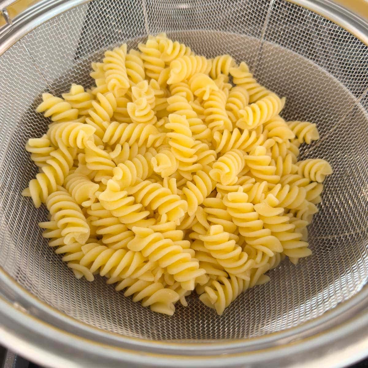 Pasta draining in a stainless steel sieve.