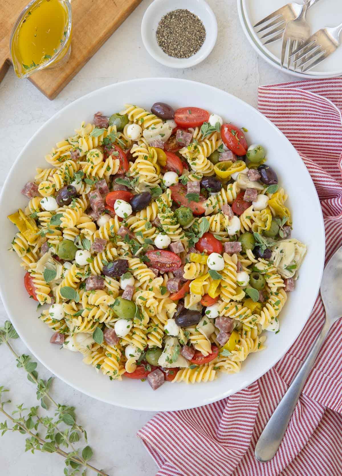 A round bowl of colorful antipasto salad with rotini pasta, tomatoes, olives, mozzarella, and herbs.