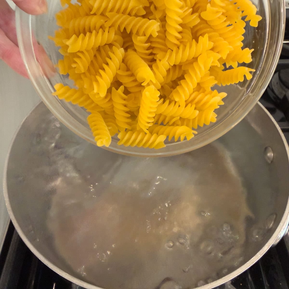 Golden rotini pasta pouring into a pot of boiling water.
