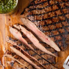 Partially sliced flank steak with perfect grill marks on a brown wood board.