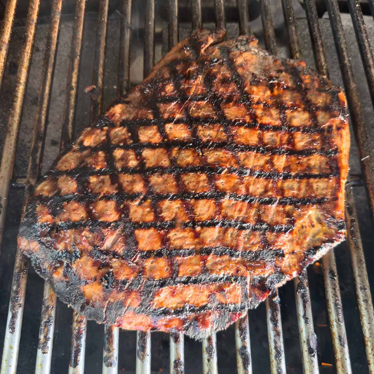 Flank steak on grill grates with perfect crosshatch grill marks.