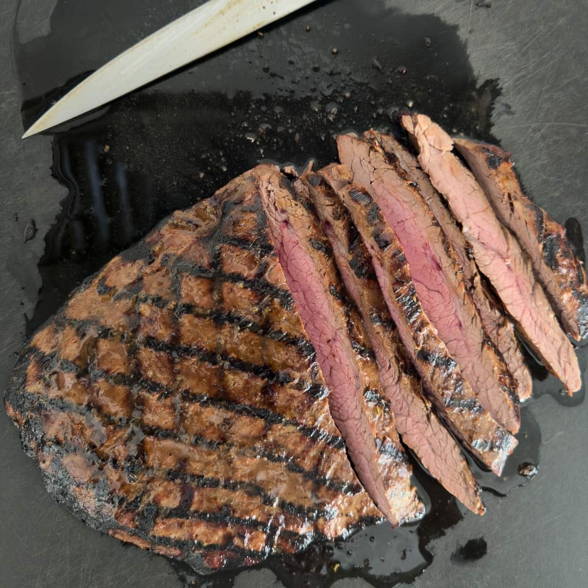 Slicing flank steak thinly across the grain pn a black cutting board.