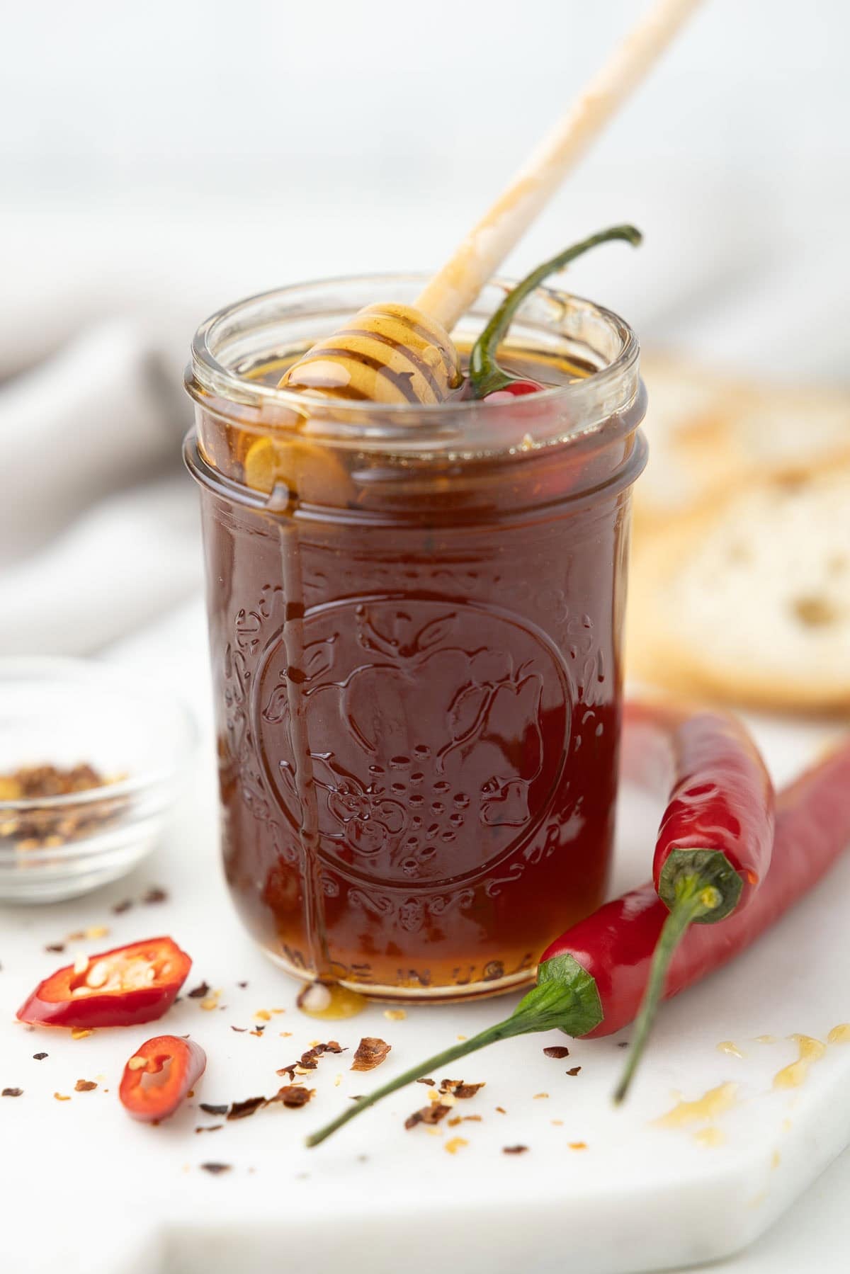 A gleaming jar of hot honey with red chile on the top and a honey drizzler.