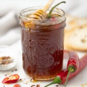 A jar of hot honey with red chile pepper and chile flakes, and honey dipper.