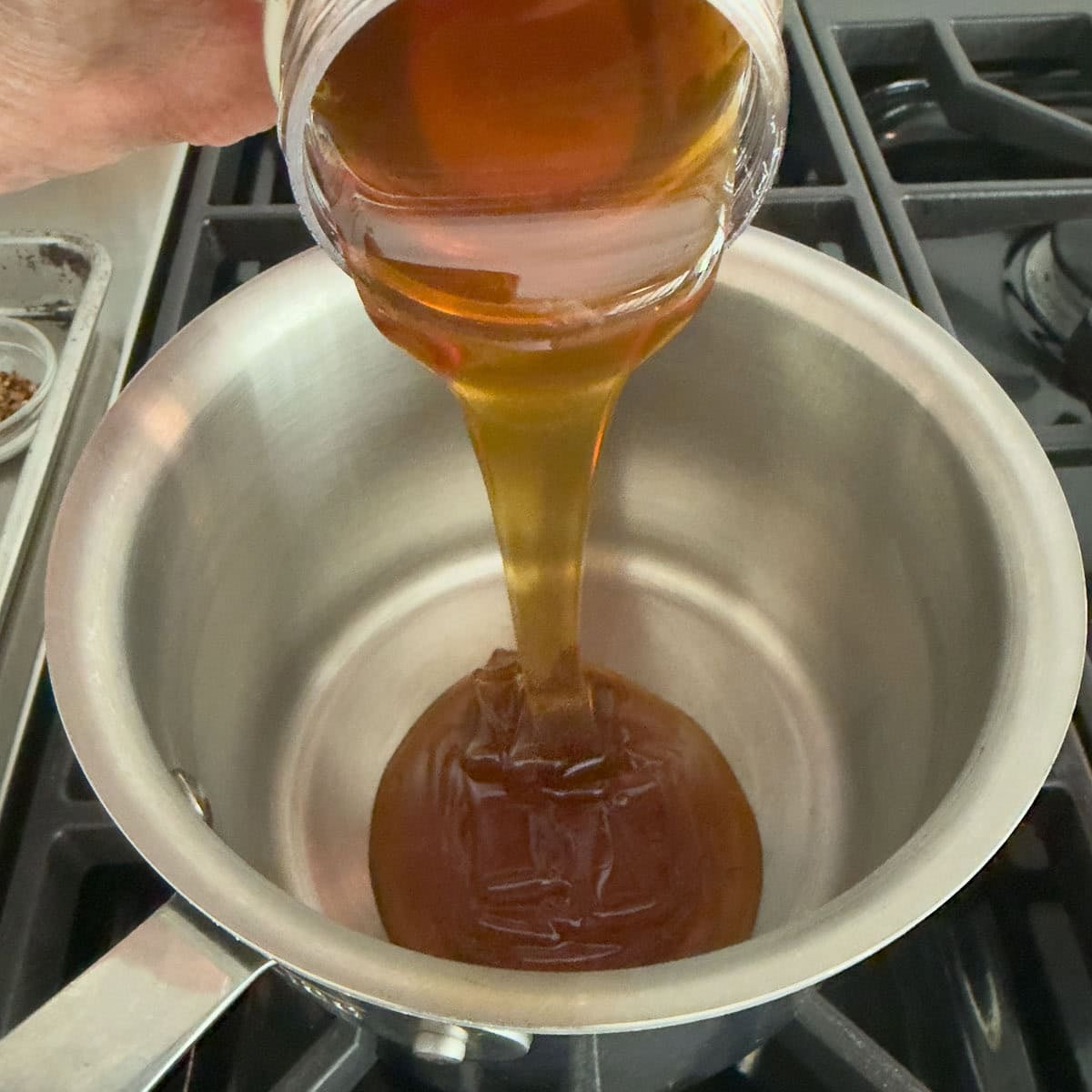 Pouring honey into a small stainless steel pan to make hot honey.