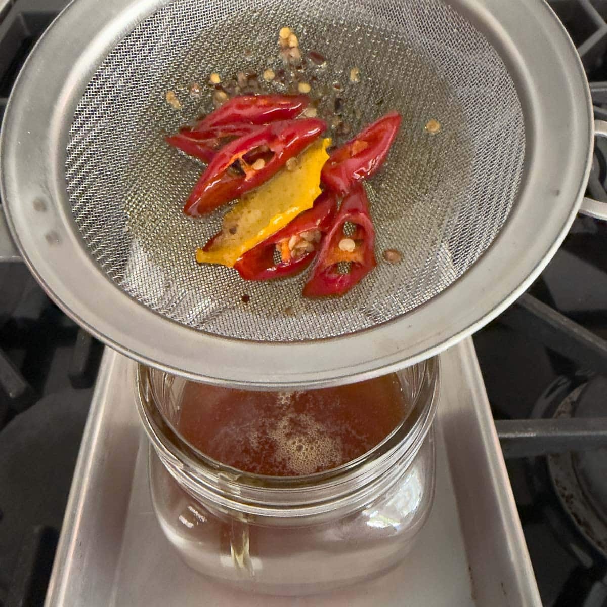 Straining infused hot honey through a fine sieve into a jar.