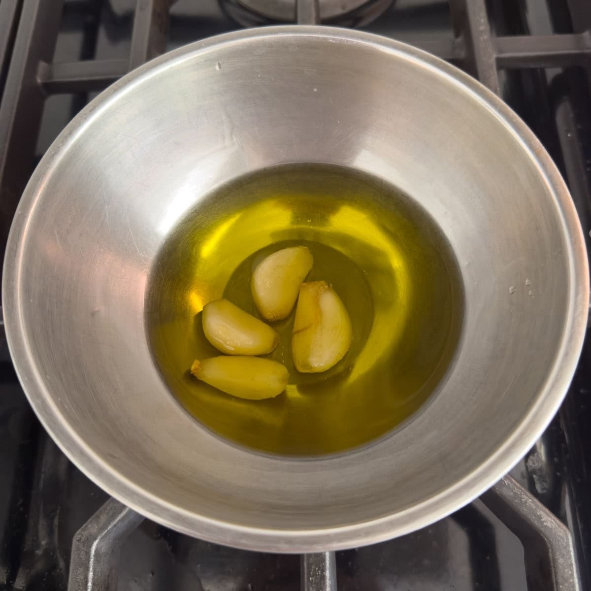 Garlic cloves in olive oil cooling in a steel bow. on a stovetop.