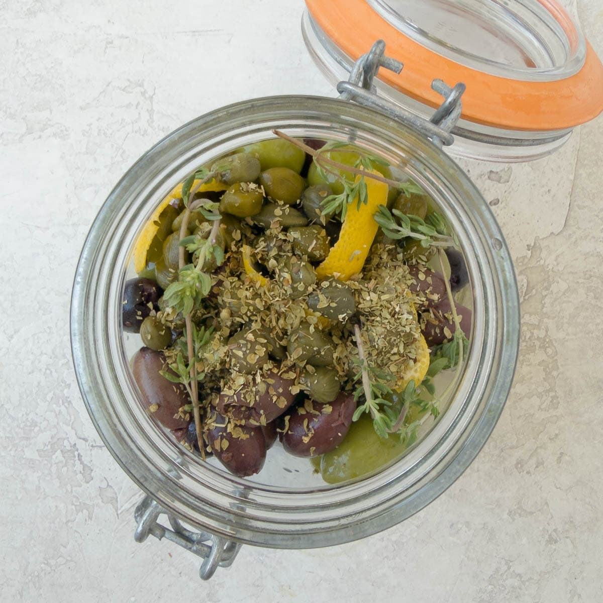 A jar filled with olives, herbs, and lemon zest.