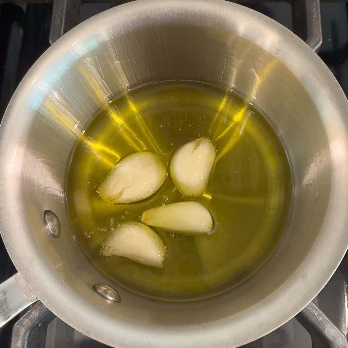 Poaching whole peeled garlic cloves in a stainless steel pan.