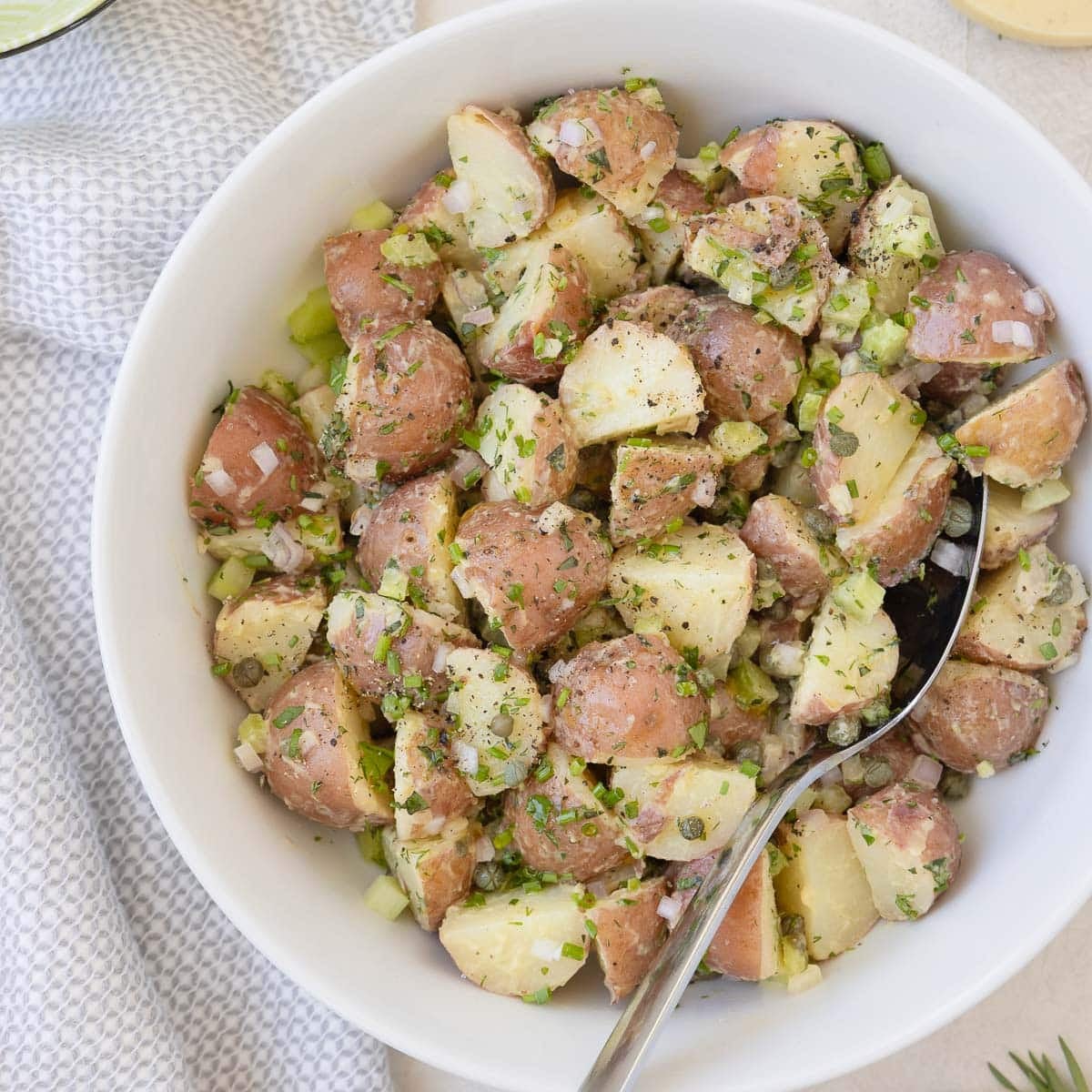 A bowl of red potato salad with a creamy dressing and a serving spoon.