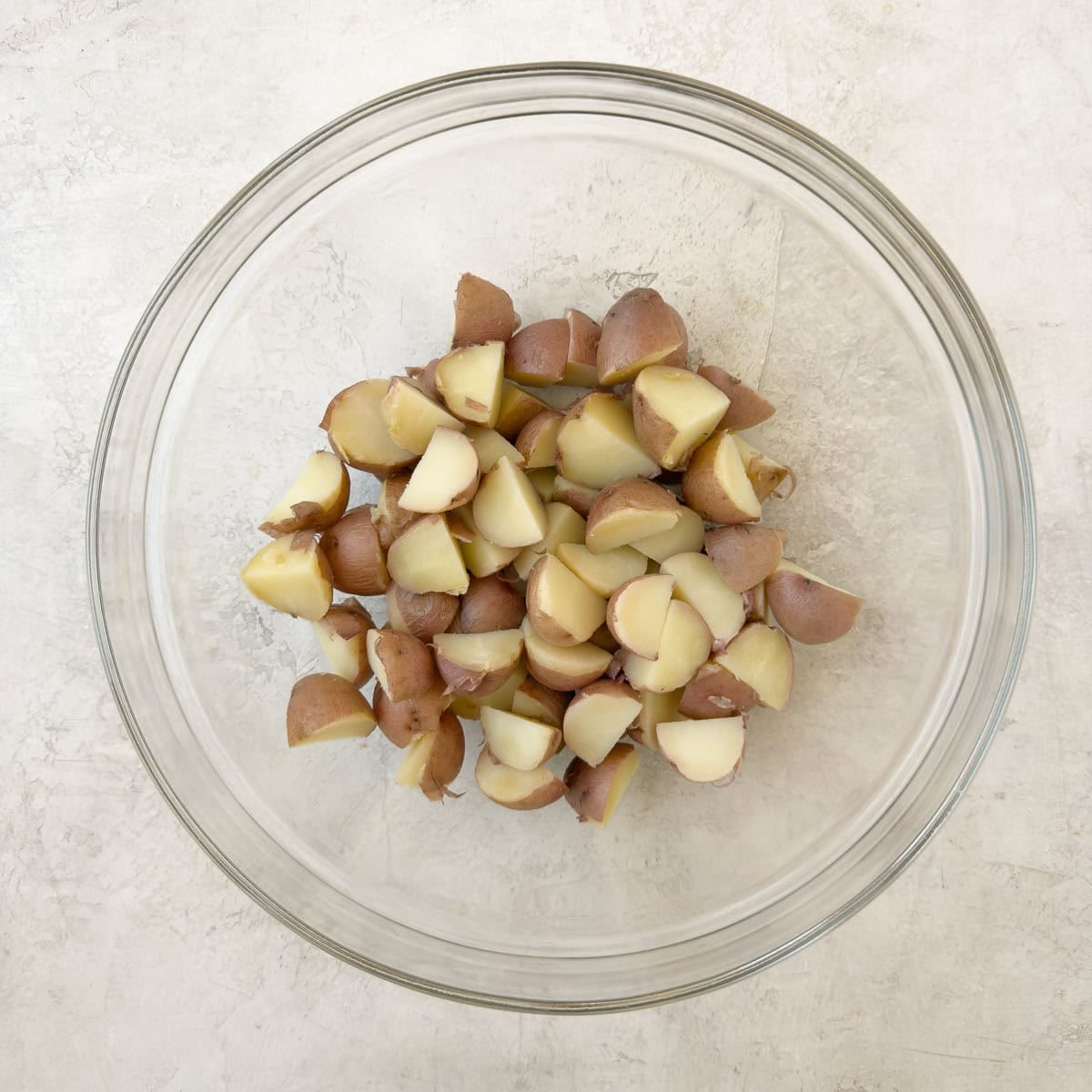 Quartered, cooked red potatoes in a glass bowl.