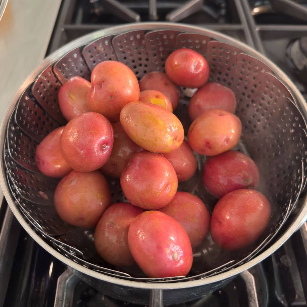 a steamer basket filled with baby red potatoes on the stovetop.