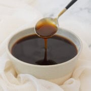 A rustic bowl of dark brown glossy teriyaki sauce with a spoon.