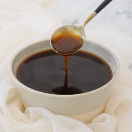 A rustic bowl of dark brown glossy teriyaki sauce with a spoon.