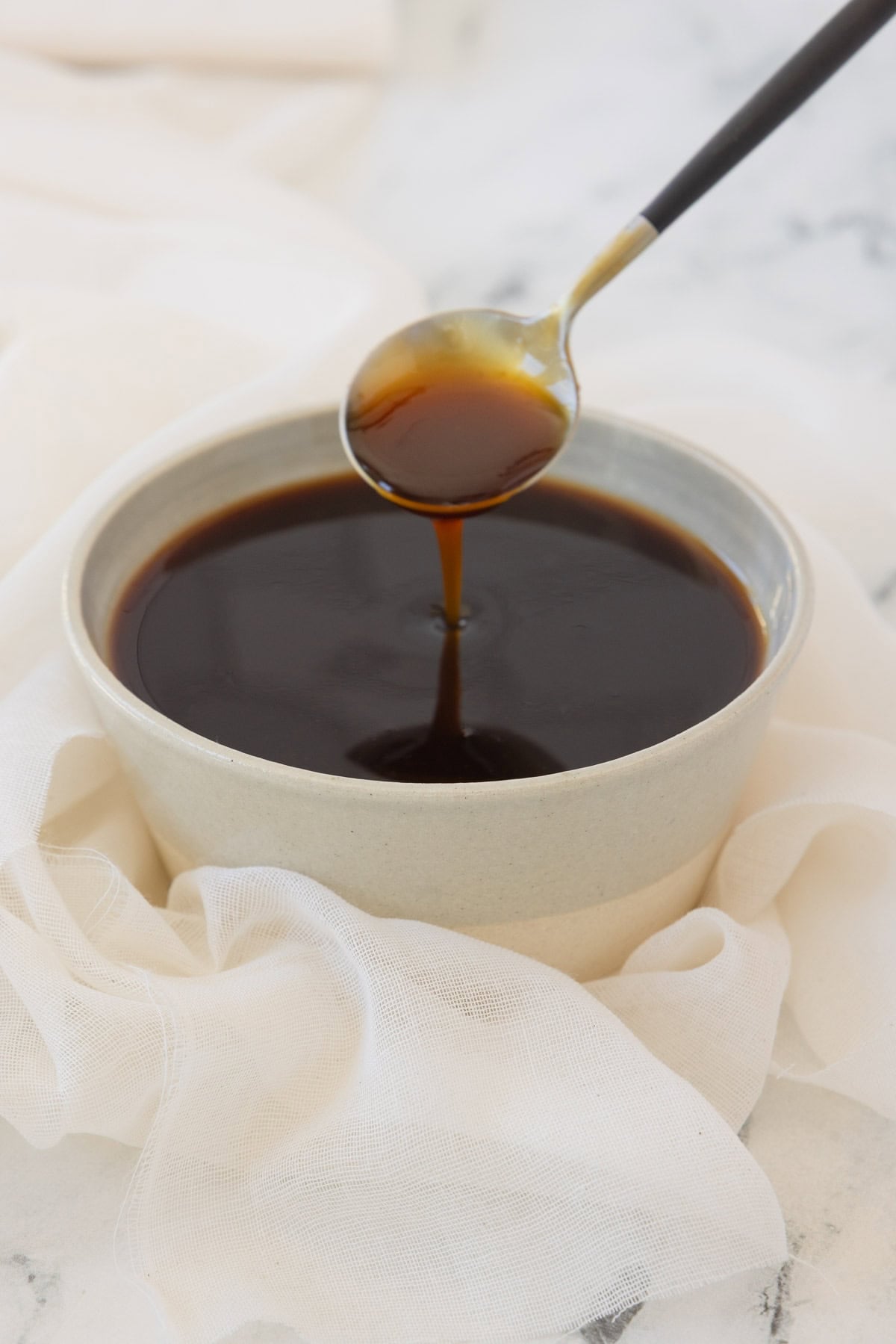 A pottery bowl filled with glossy dark teriyaki sauce dripping off a spoon.