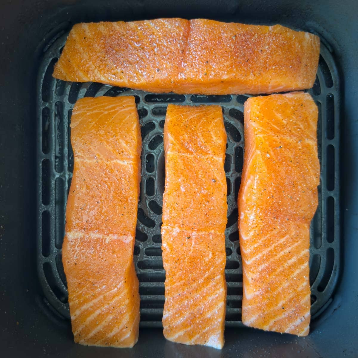 Air fryer salmon fillets seasoned, and ready for air frying in the basket.