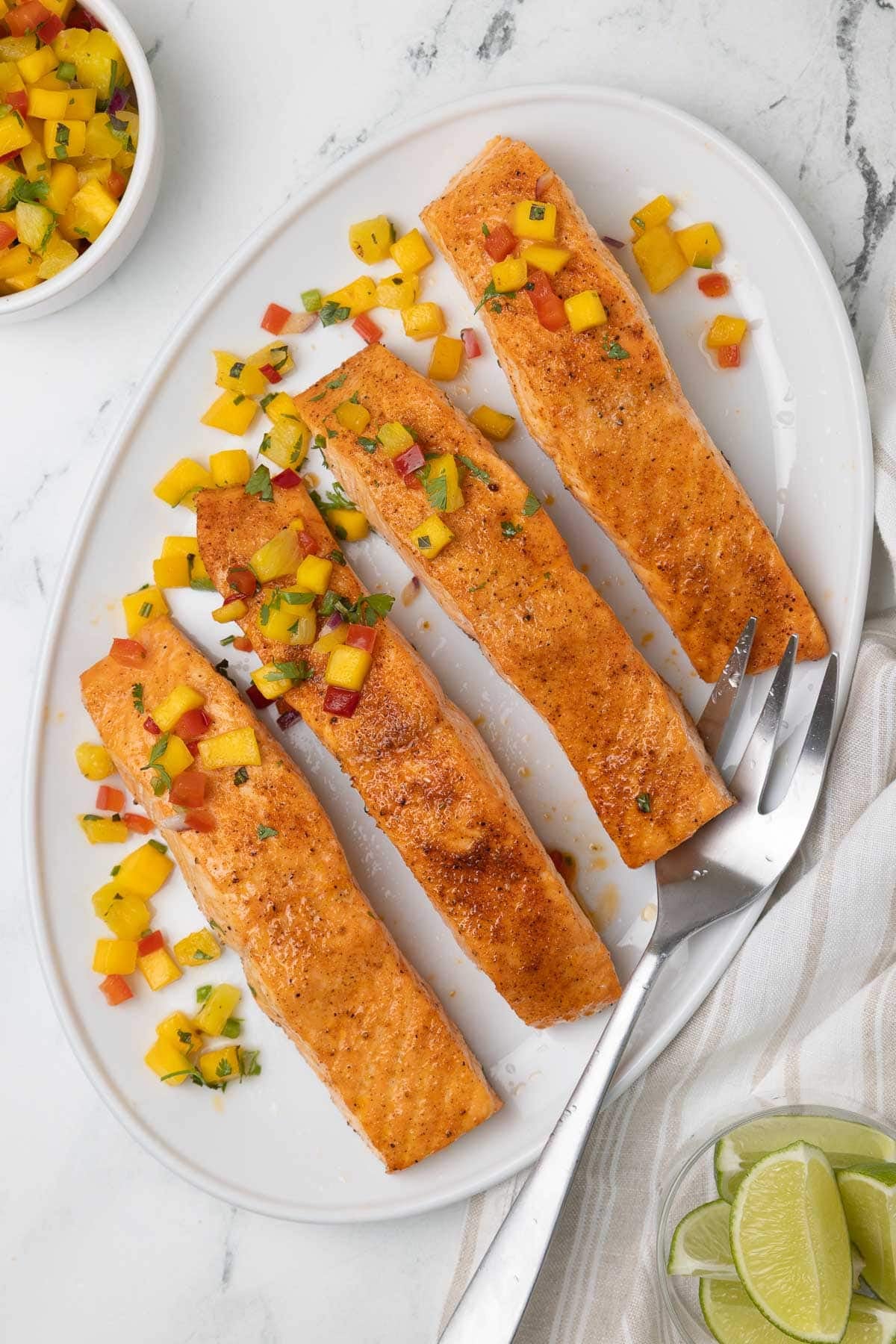A white platter of air fryer salmon fillets topped with a pineapple mango salsa. 