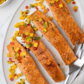 An oval plate of bright orange salmon fillets for serving with pineapple salsa.