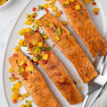 An oval plate of bright orange salmon fillets for serving with pineapple salsa.