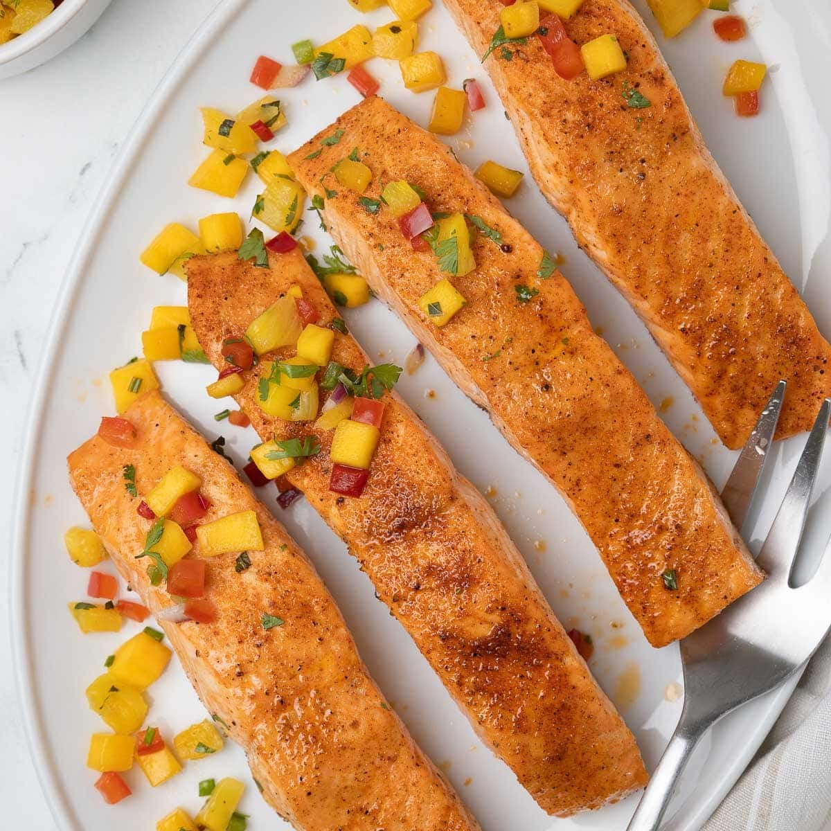 An oval plate of bright orange salmon fillets for serving with pineapple salsa.
