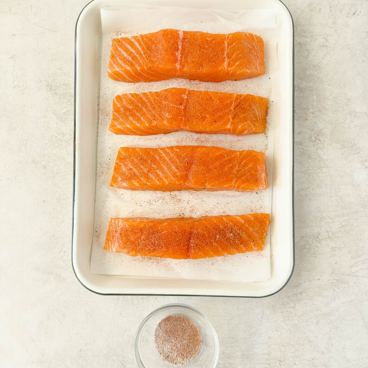Seasoning salmon fillets on a white tray before air frying salmon.