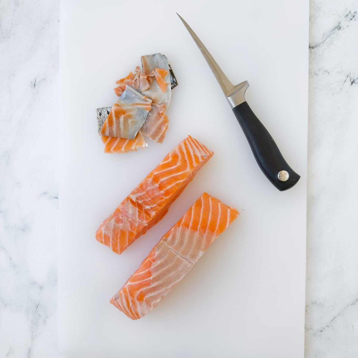 Skining salmon fillets and removing the blood line on a white cutting board.