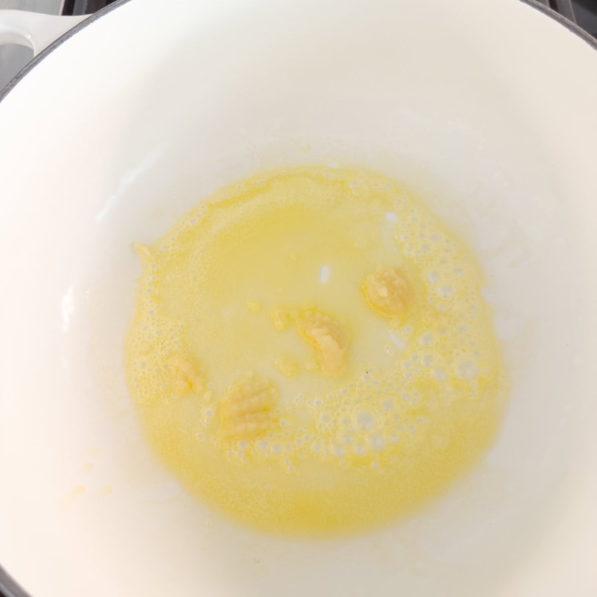 Cooking garlic in melted butter in a white pot.