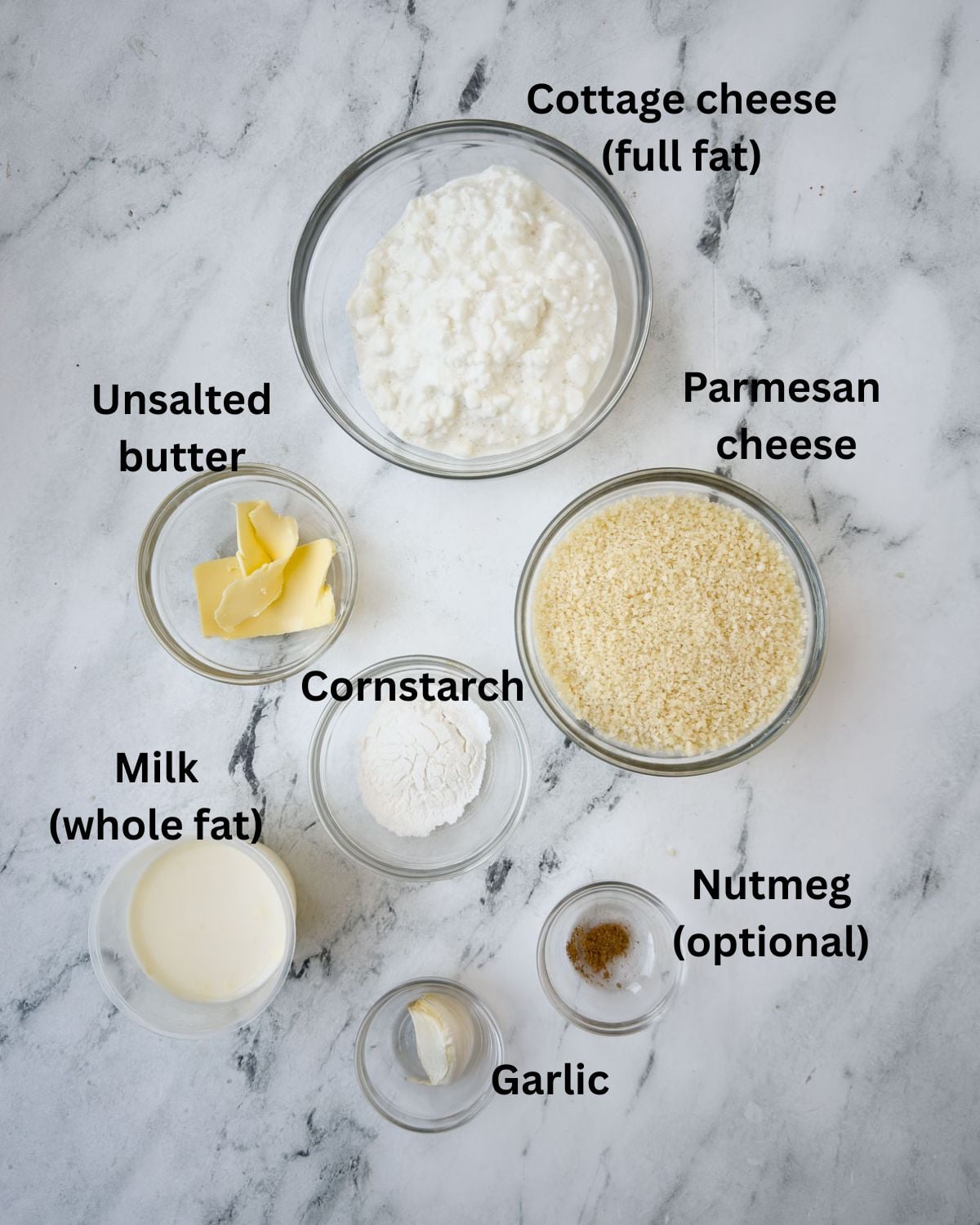 Ingredients for cottage cheese alfredo sauce in prep bowls on a marble counter.