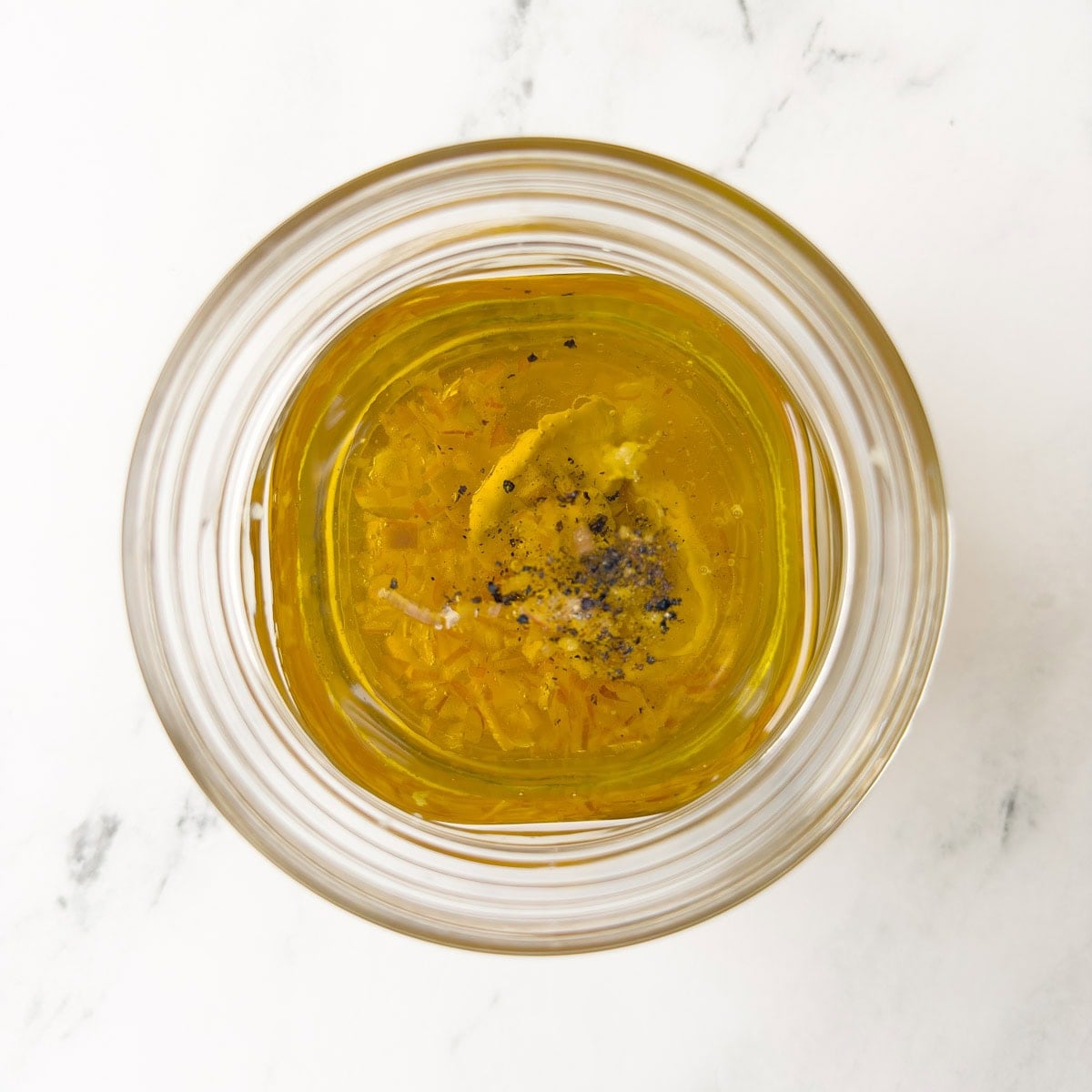 Olive oil, vinegar, Dijon mustard, garlic, shallot, and pepper in a jar for dressing.