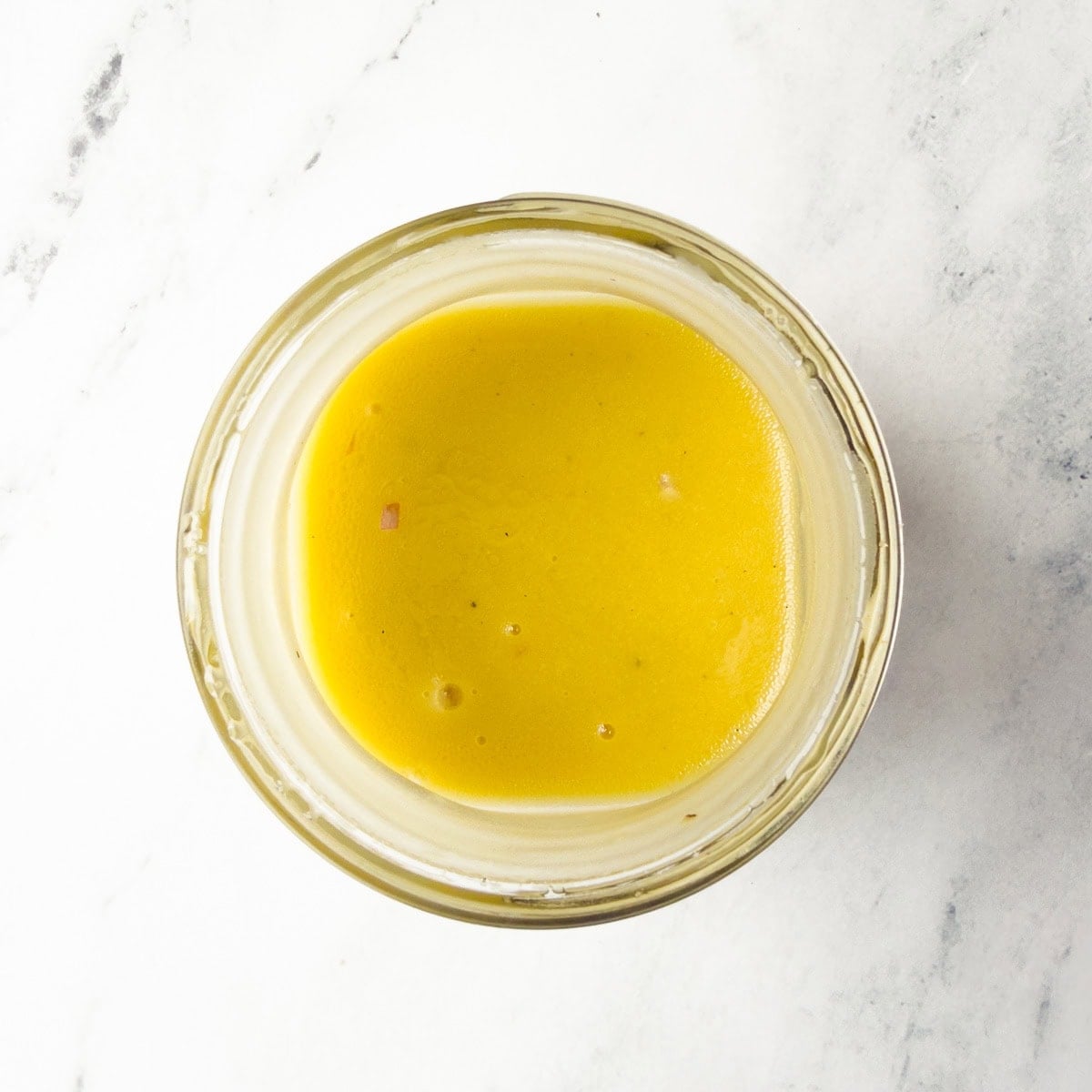 Creamy and bright yellow, Dijon mustard vinaigrette ready to serve in a glass jar.
