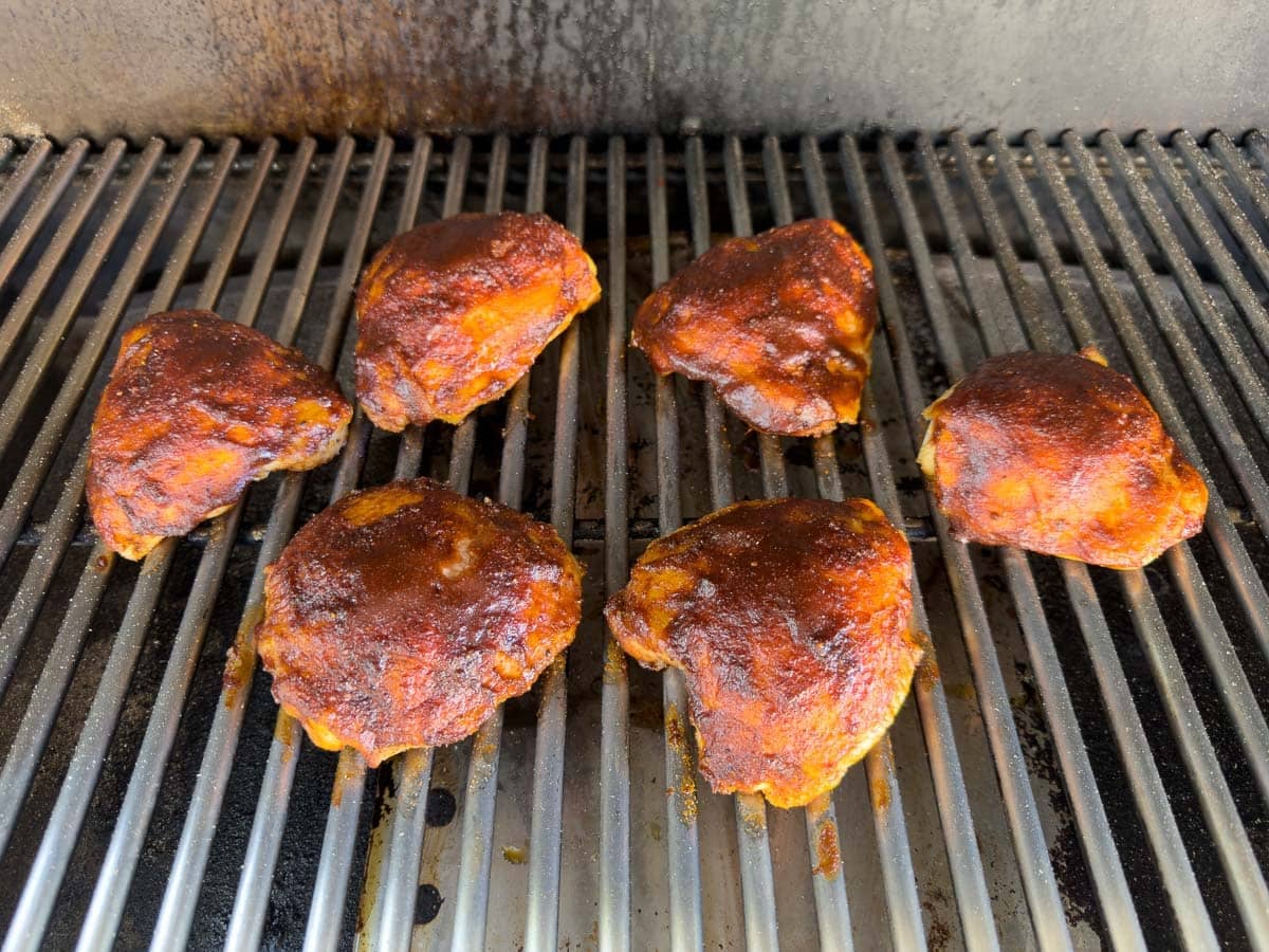 Smoked chicken thighs almost done, glazed with bbq sauce on grill grates.