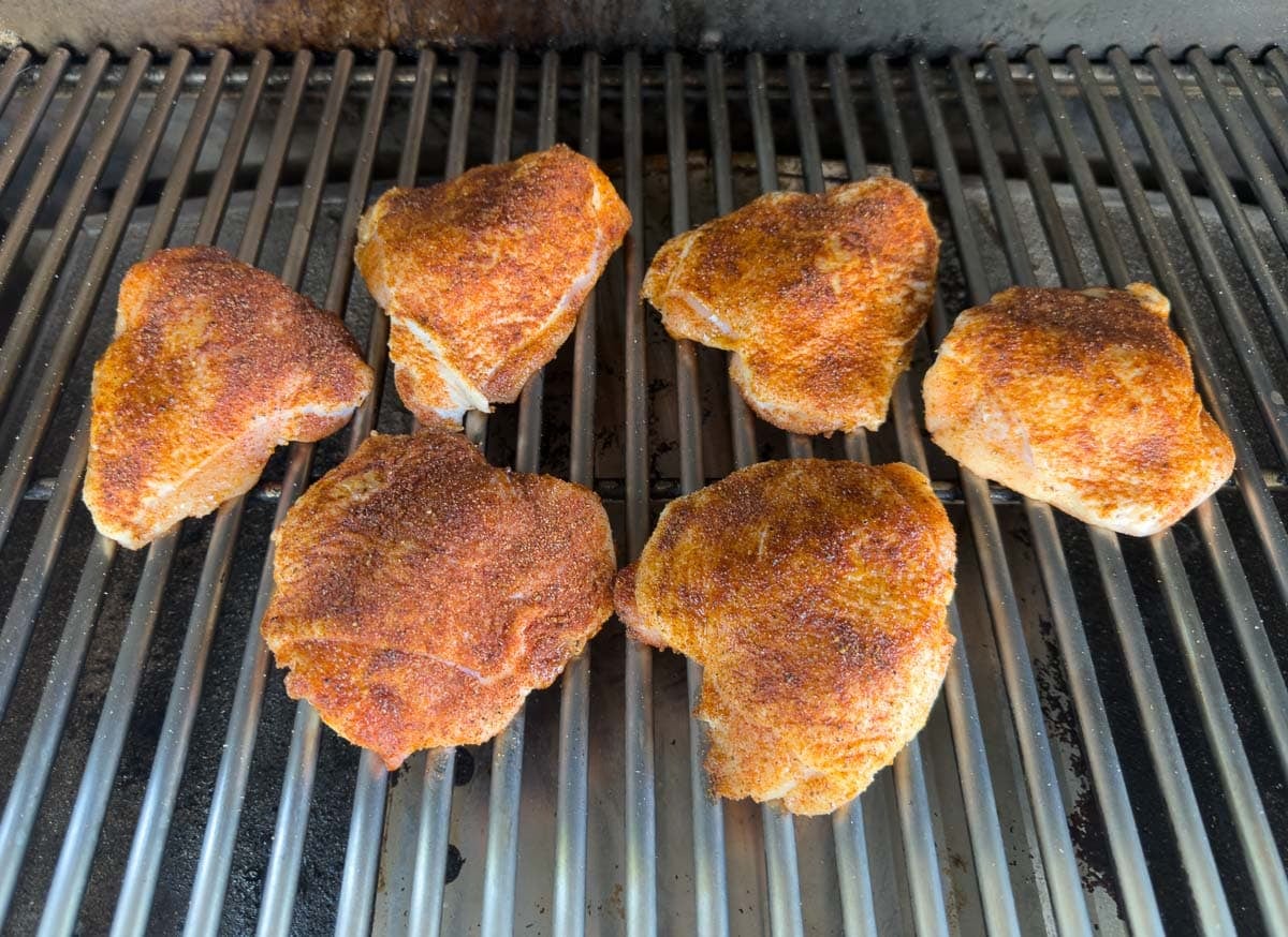 Dry rub seasoned chicken thighs on grill grates.
