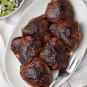 A platter of smoked chicken thighs with a dark glossy bbq glaze and salad on the side.