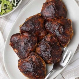 A platter of smoked chicken thighs with a dark glossy bbq glaze and salad on the side.