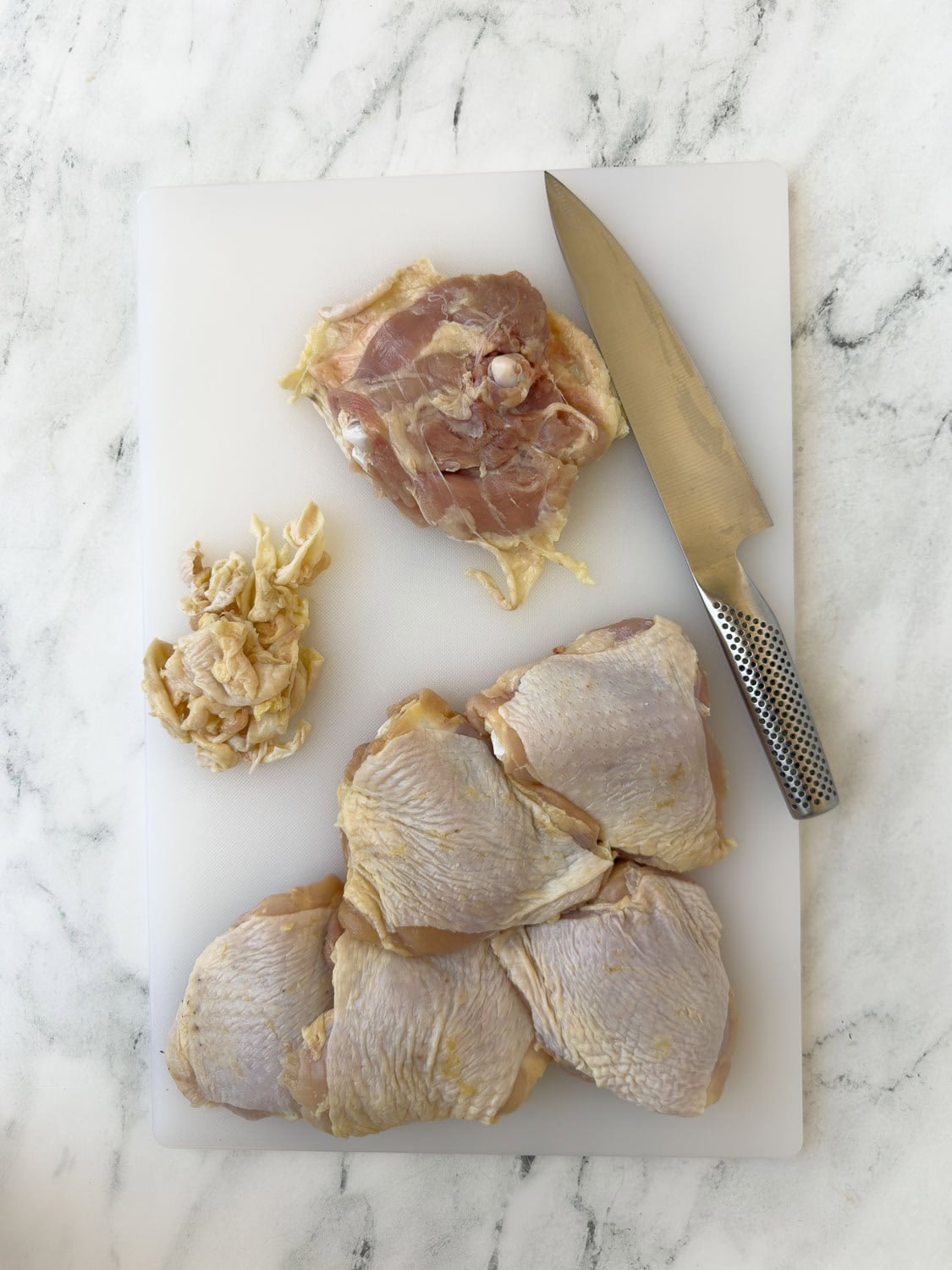 Chicken thighs being trimmed of excess fat with a chefs knife.
