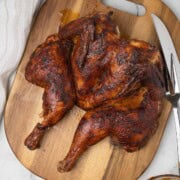 Smoked spatchcock chicken on a wood cutting board with a carving knife.