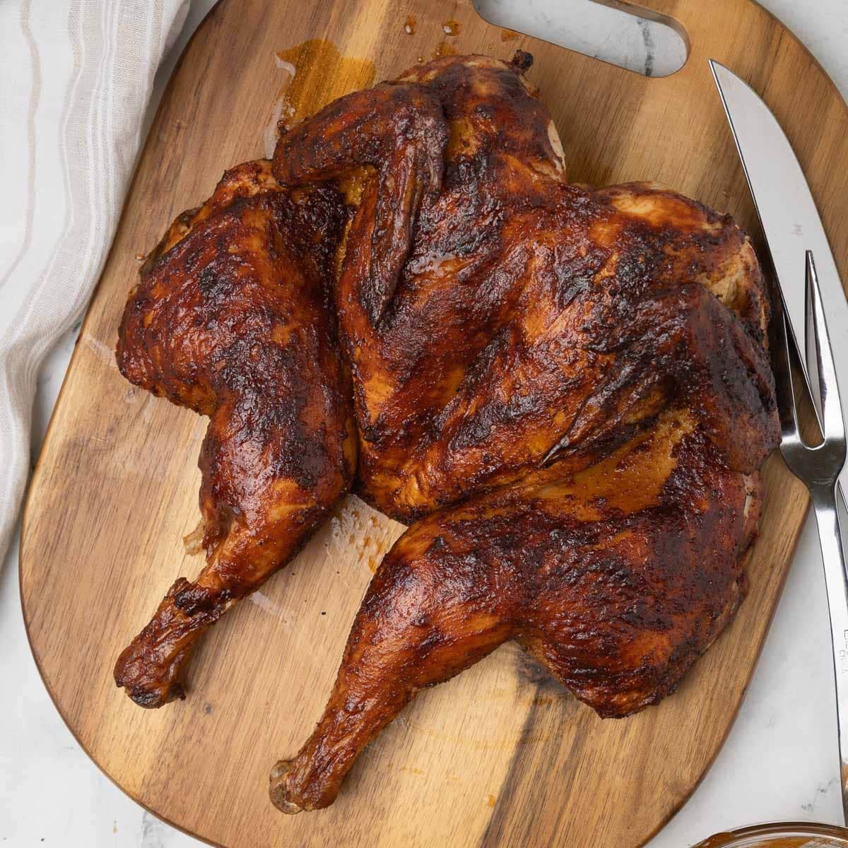 Smoked spatchcock chicken on a wood cutting board with a carving knife.