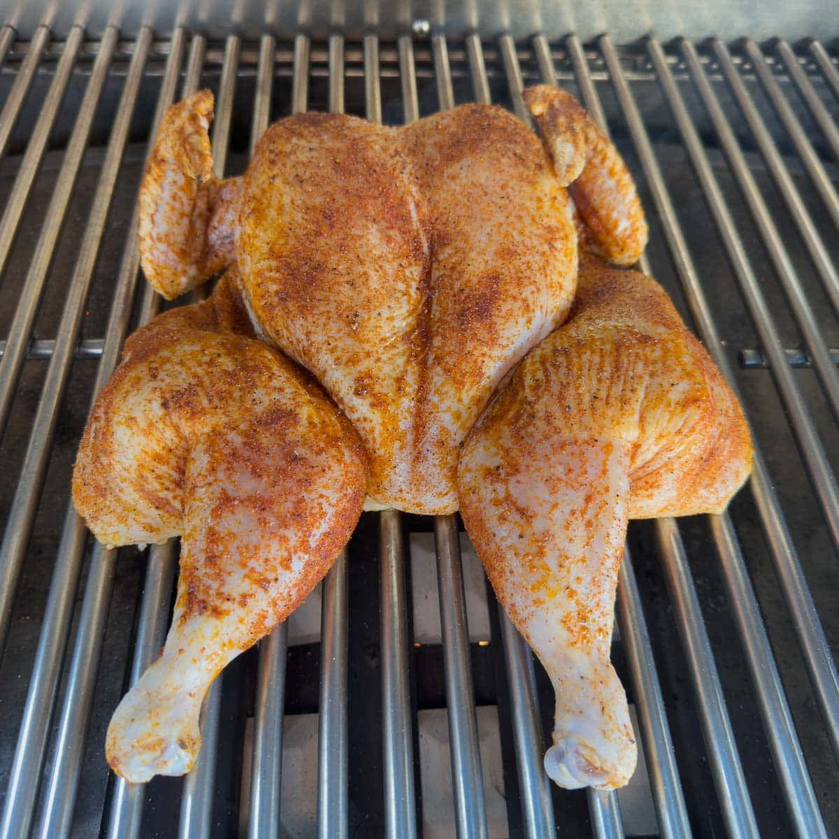 a whole spatchcocked chicken coated with dry rub on grill grates.