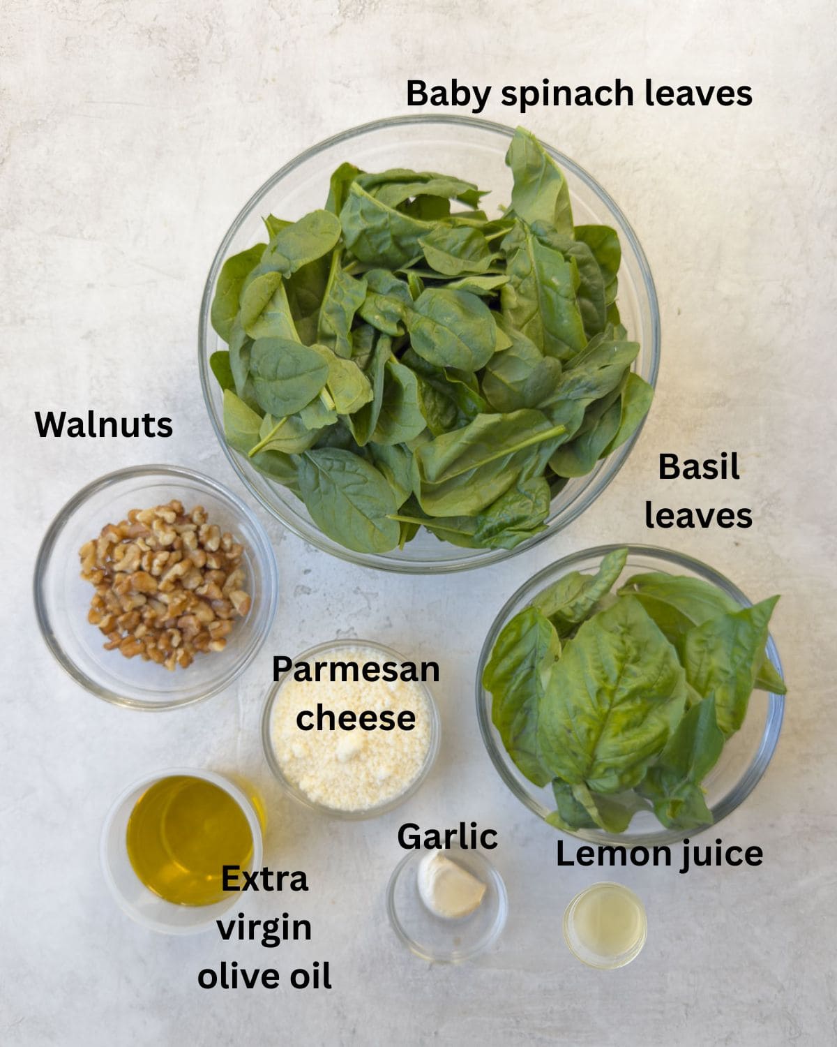 Ingredients for a spinach pesto in prep bowls on a counter.