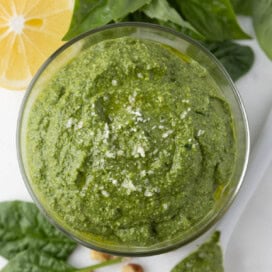 A glass jar of bright grren spinach pesto with basil, lemon, parmesan , and walnuts, ready to enjoy.