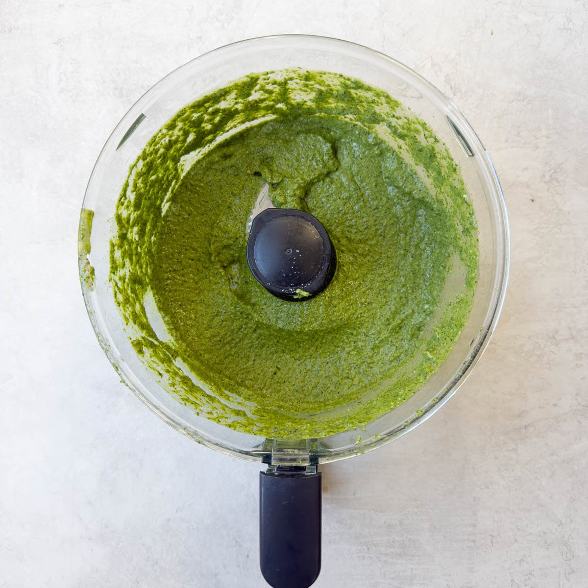 A vivid green spinach pesto pureed in a food processor, ready to serve.