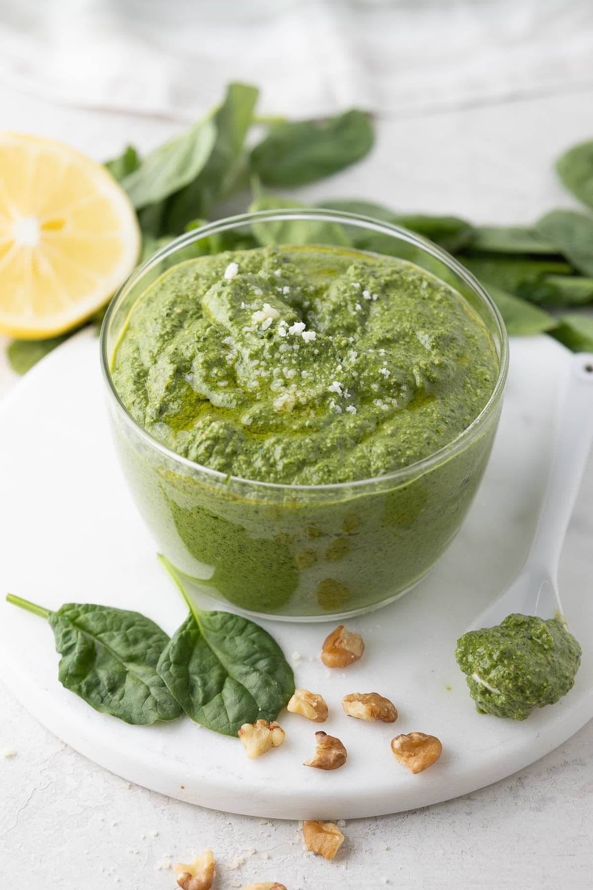 A vivid green bowl of creamy spinach pesto sprinkled with parmesan, lemon half behind.