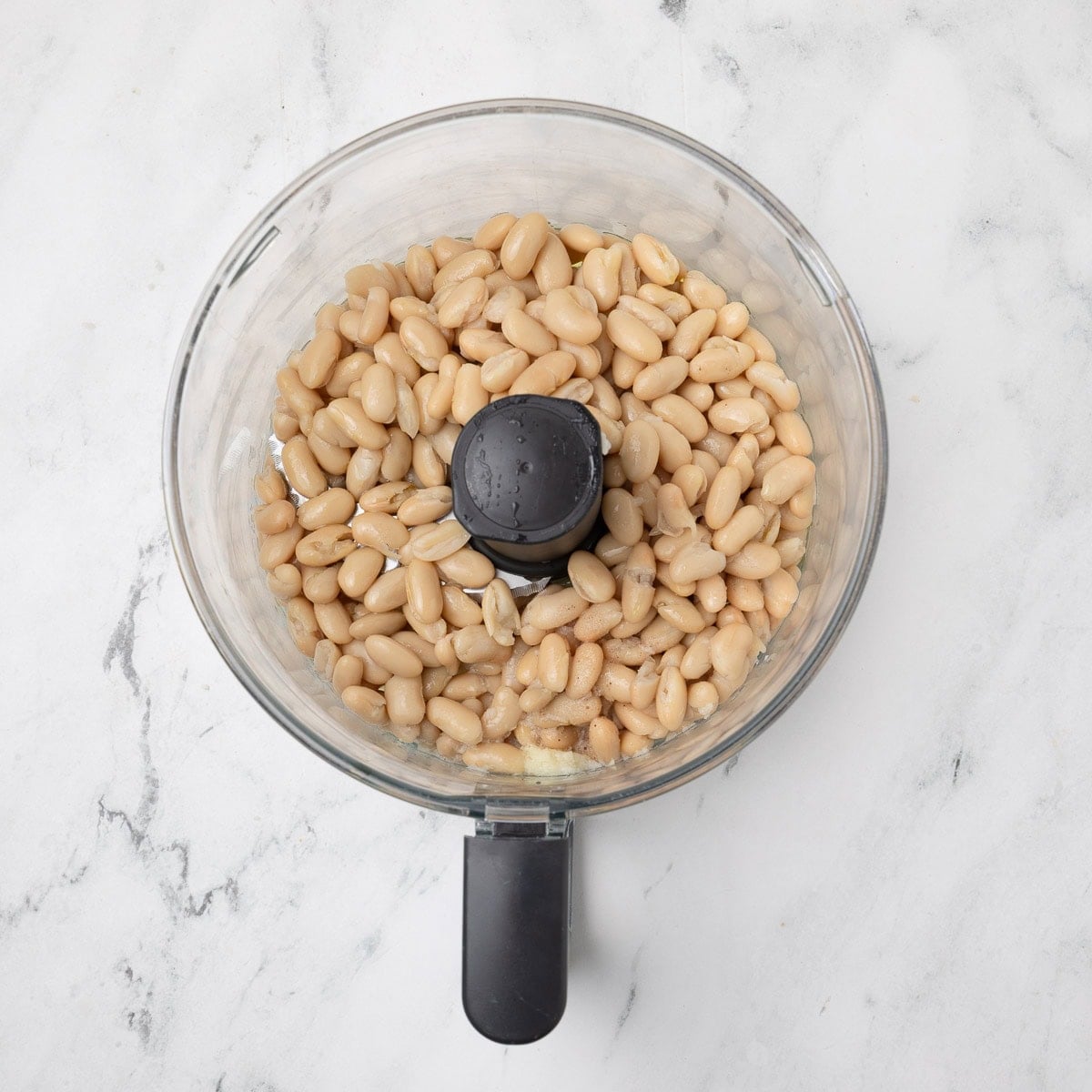 Rinsed and drained cannellini beans in a food processor workbowl.
