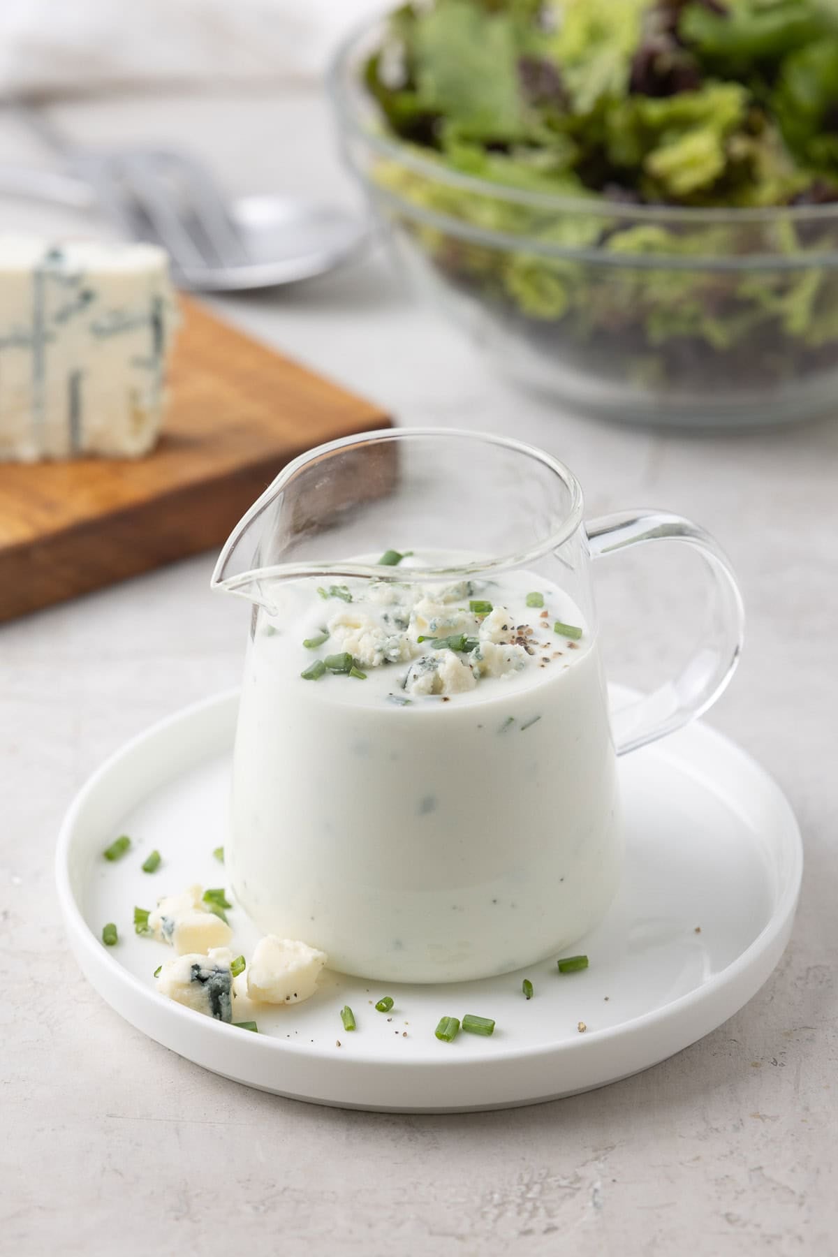 A small glass pitcher of yogurt blue cheese dressing with chive and blue crumbles.