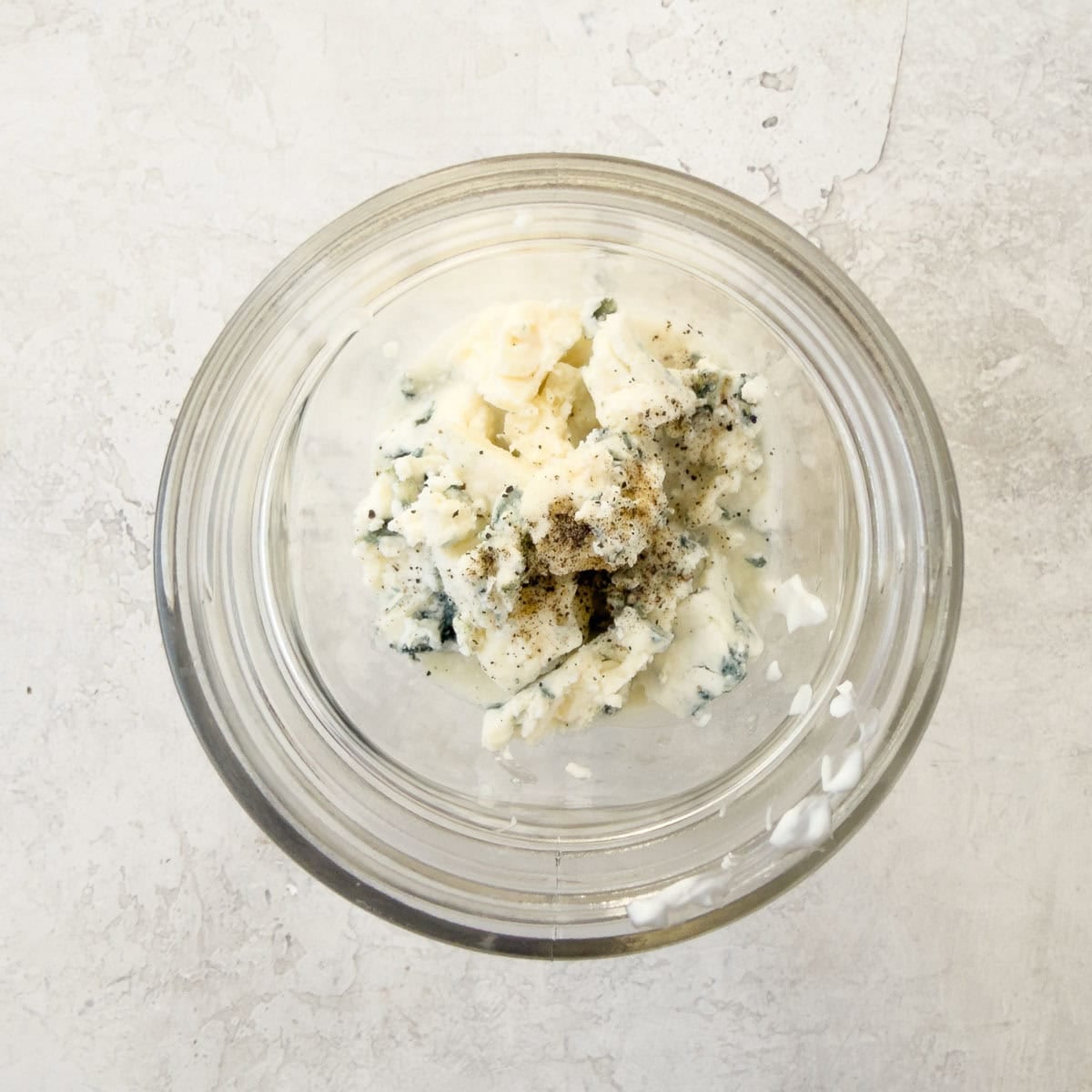 Blue cheese, mayo, yogurt, and pepper in a small blender jar for making blue cheese dressing.