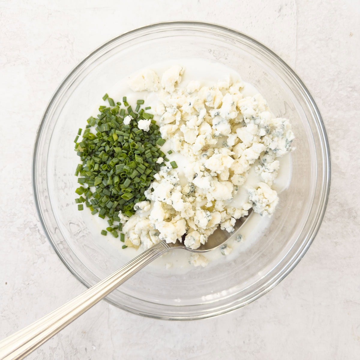 Blue cheese dressing base, blue cheese crumbles and chives in a glass bowl.