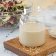 Creamy sesame ginger dressing in a small jar on a mini cutting board with white sesame seeds.