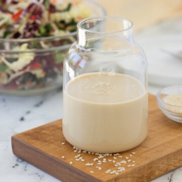 Creamy sesame ginger dressing in a small jar on a mini cutting board with white sesame seeds.