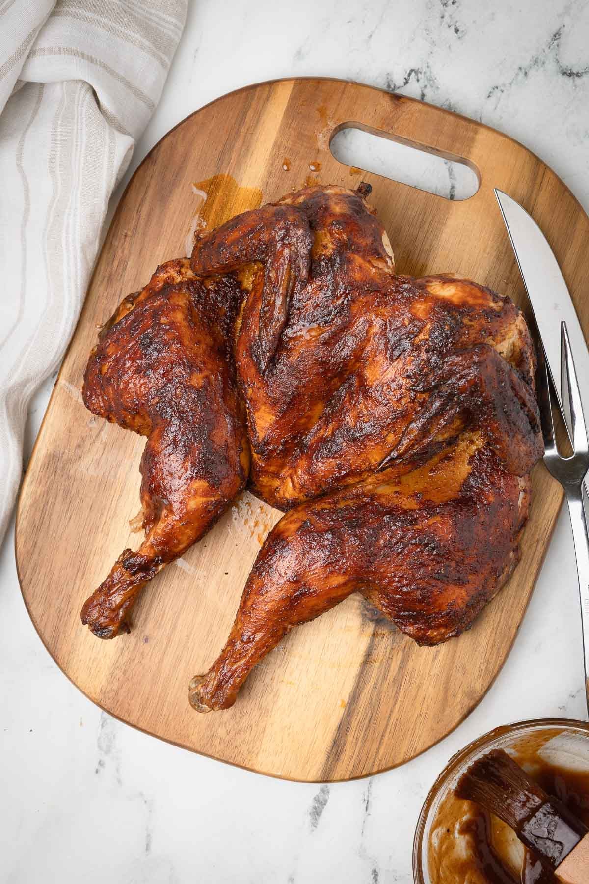 A juicy, burnished, smoked spatchcock chicken just off the grill with carving knife, fork, and bbq glaze.