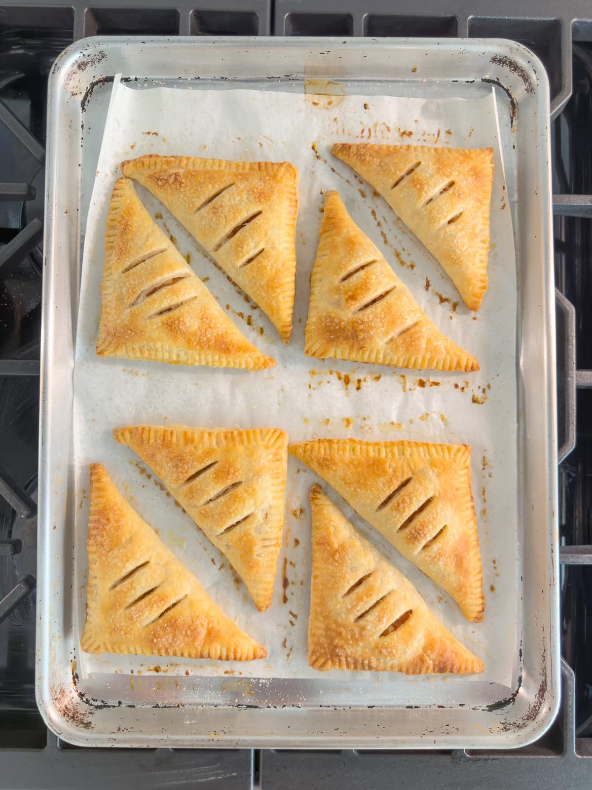 A baking tray of golden apple turnovers in puff pastry cooling before glazing.